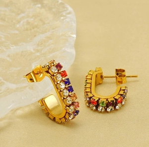 Close-up of gold-plated U-shaped earrings with colorful square zircon stones on glass