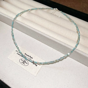 Detailed view of a gold-plated pearl necklace with blue and white beads in a gift box