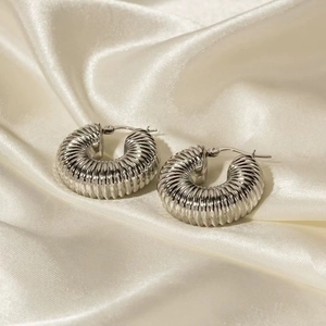 Polished silver stainless steel ribbed hoop earrings resting on elegant cream satin fabric