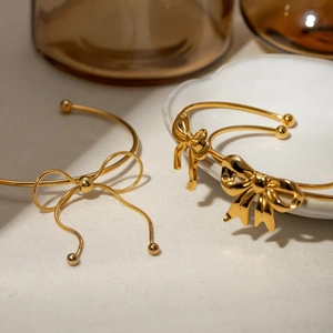 Minimalist gold bow open cuff bracelet in stainless steel displayed on a white plate