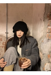 Close-up of black knit beanie styled with a dark grey blazer in a vintage industrial setting