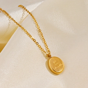 Gold plated stainless steel necklace with engraved oval pendant on silk background