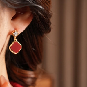 Macro shot of 18k gold plated diamond-shaped red earrings with zircon studs on ear