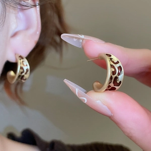 Détail de boucles d'oreilles créoles léopard en émail marron et métal doré sur modèle