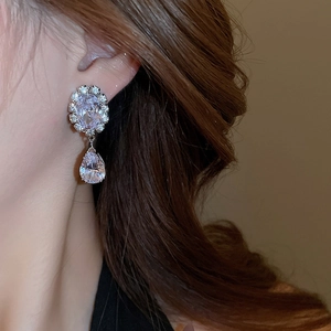 Close-up of sparkling pear-cut zircon drop earrings worn on ear with silver finish