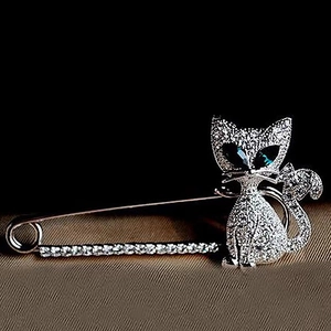 Silver cat brooch with emerald eyes and sparkling crystals on brown fabric texture