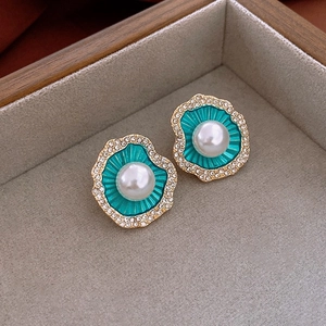 Macro shot of vintage gold-plated pearl earrings with green enamel and crystal trim