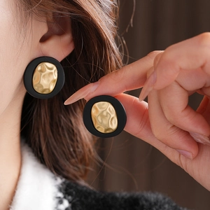 Macro detail of round black and gold hammered texture earrings on female model
