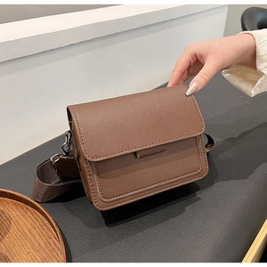 Detail view of a vintage dark brown square bag with a wide woven strap on a leather seat