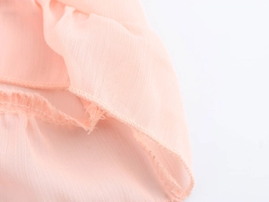 Close-up of light pink chiffon fabric showing ruffle details and hemline stitching