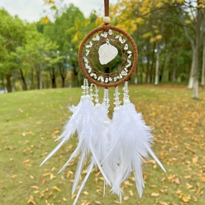Detail of dream catcher with white feathers and natural stone hanging on a tree branch