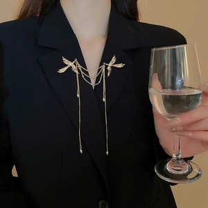 Dettaglio della spilla a fenice dorata con nappe di perle su un blazer nero di lusso