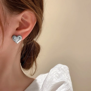 Close-up of a silver heart stud earring worn by a model with polished finish details