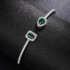 Detail of silver open bangle featuring green teardrop and rectangular cubic zirconia stones