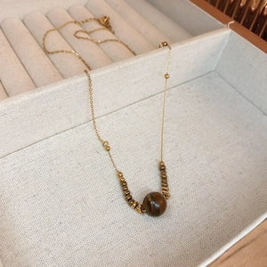 Detailed close-up of a golden beaded necklace with a natural tiger eye stone pendant