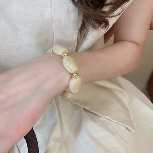 Macro shot of oval cream resin beads with marble texture and gold spacers on a bracelet