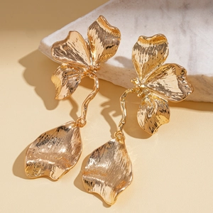 Detailed view of golden flower earrings with textured petals on marble surface