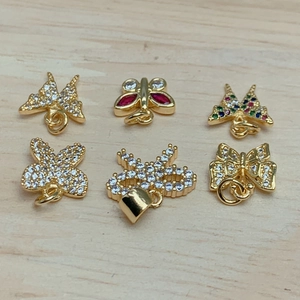 Detailed view of six gold butterfly and bow pendants with vibrant zircon stones on wood