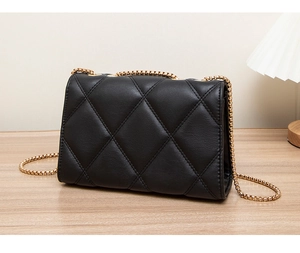 Close-up of quilted black leather shoulder bag with golden chain strap on a wooden desk