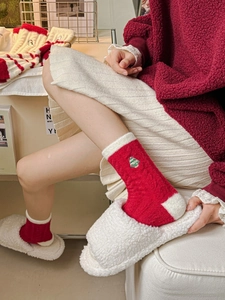Detail of red Christmas socks with tree embroidery paired with white plush slippers