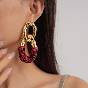 Close-up of geometric gold metal and red-black leather wrapped earrings on a model