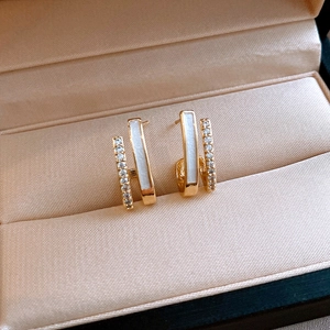 Macro shot of gold double-row C-shaped earrings with white enamel and sparkling zircon