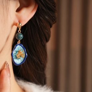 Close-up of vintage flower drop earring with blue marble bead and golden stud on model