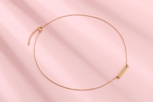 Macro view of gold bar necklace featuring small purple stone over pink background