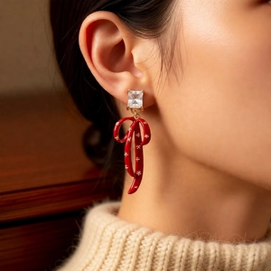 Detail of red bow earrings with square crystal and gold star accents on model