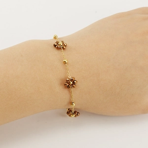 Golden stainless steel floral bracelet with faceted brown beads shown on model wrist