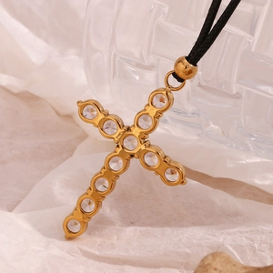 Macro shot of gold cross pendant with clear cubic zirconia on a black cord necklace