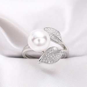 Eleganter Silberring mit Blättern und weißer Perle auf weichem Seidenhintergrund