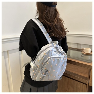 Detailed view of floral pattern gray backpack worn by model in a cozy interior setting