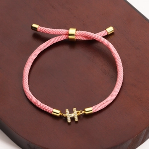 Detailed view of pink braided rope bracelet with a gold crystal-encrusted H charm