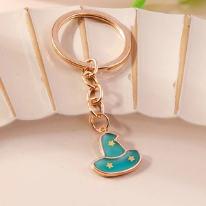 Detailed view of a green enamel witch hat keychain with yellow stars on a beige surface