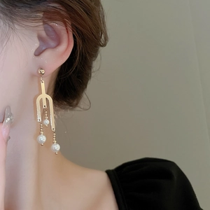 Detail of golden U-shaped pearl drop earrings on a model showing the elegant dangle