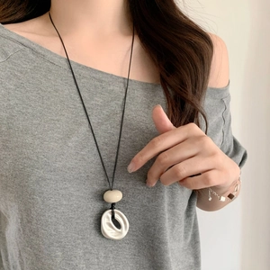 Detail of geometric pendant necklace showing irregular white ring and beige oval bead