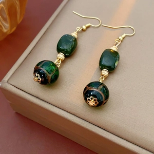 Close-up of vintage earrings featuring green resin beads and black patterned accents