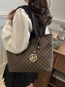 Brown monogram tote bag with M pattern and gold pendant shown on model in street style