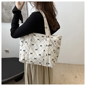 Detailed view of beige quilted corduroy tote bag with black bow patterns on shoulder