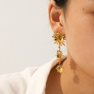 Detailed view of 18k gold plated stainless steel sun drop earrings on a model ear