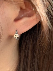 Close-up of minimalist silver smiley face charm earrings worn on ear with round hoop