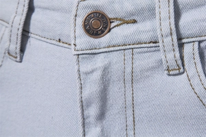 Macro shot of bronze metal button with Jeans engraving on light blue denim trousers