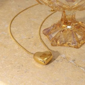 Minimalist gold heart pendant necklace with sleek snake chain on marble background