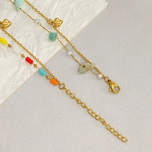 Detail of gold chain bracelet with heart charm, pearls and colorful natural stones