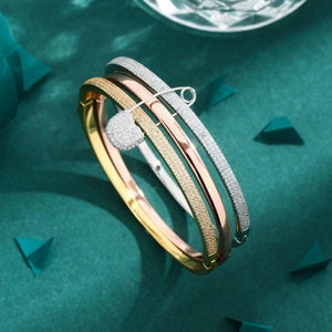 Three-tone stackable crystal-pave rings with a safety pin charm on green background