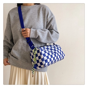 Blue checkerboard canvas cylinder bag featuring a wide strap and green tassel charm