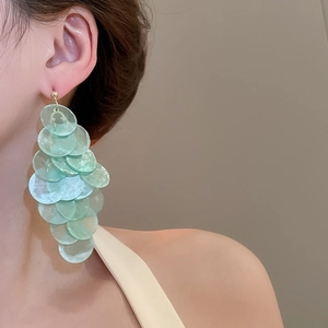Detail of mint green translucent shell fringe earrings on model with warm background