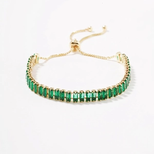 Detail view of gold adjustable bracelet with rectangular emerald green cubic zirconia stones