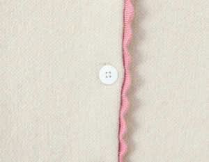 Close-up of knit texture with pink scalloped edges and glossy white button detail